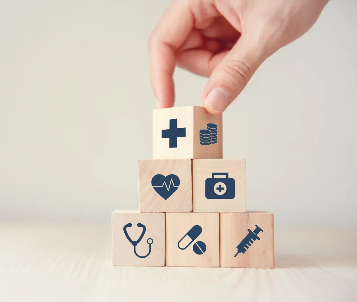 Eine Hand legt Holzwürfel mit Symbolen wie Herzmedizin und Gesundheit übereinander